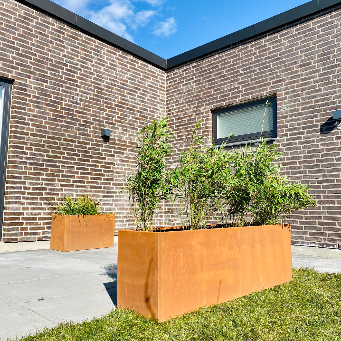 Cortenstål højbed plantet på gras med terrasse i baggrunden